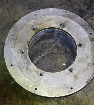 Detached circular metal flange component after soot removal during industrial fire remediation.