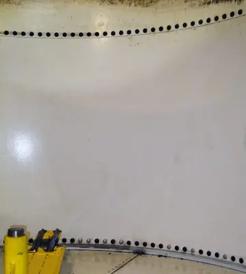 Cleaned white interior wall of an industrial tank with rows of rivets visible after fire remediation.