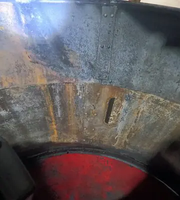 Interior of a large industrial hay grinder showing soot-covered metal surfaces and mechanical components before cleaning.