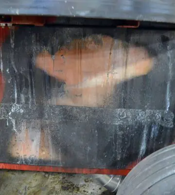 Red industrial hay grinder with a large exterior panel heavily darkened by soot and fire residue.