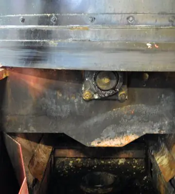 Recessed interior section of red industrial equipment heavily coated with soot before cleaning.