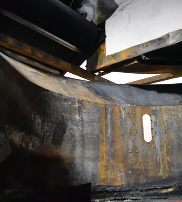 Curved interior metal surface heavily coated with soot and fire residue before cleaning.