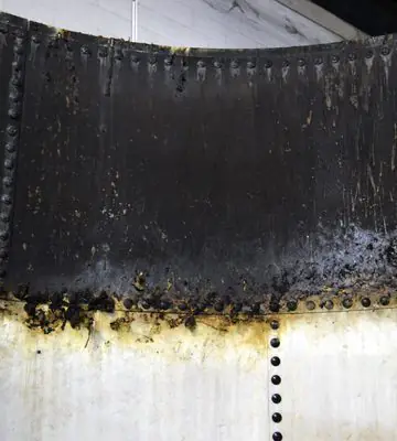 Close-up of heavy black soot and fire residue along the upper wall of a white industrial tank.