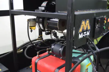 Close-up of trailer-mounted pressure washing equipment with pump, hoses, and fuel tanks.